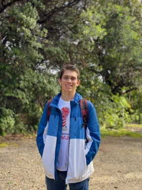 Martin wearing a jacket and a backpack in front of a green landscape